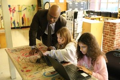 Superintendent Dr. Jones asking students about their work, students showing their work on a laptop